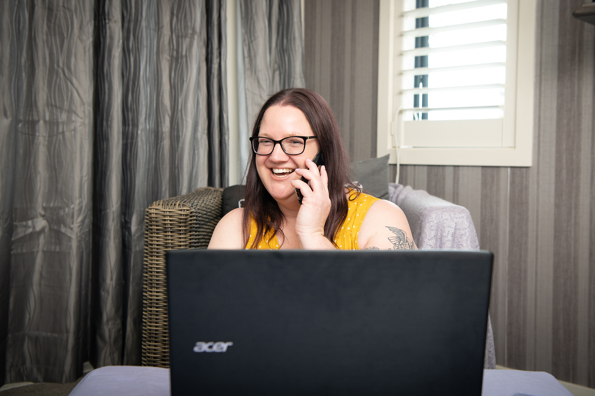 A lady sitting behind a laptop, taking a mobile call.